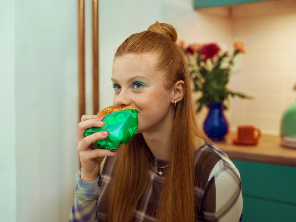 A girl with long red hair eats a hamburger