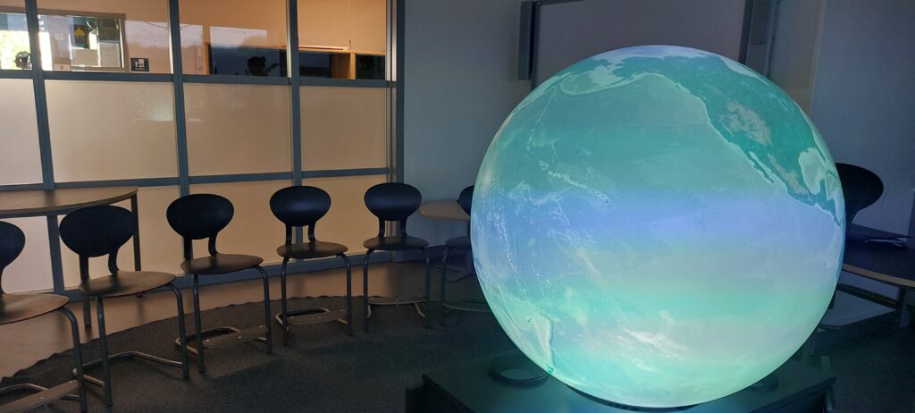 TellUs-globen placerad i ett klassrum. Stolar står i en halvcirkel bakom globen.